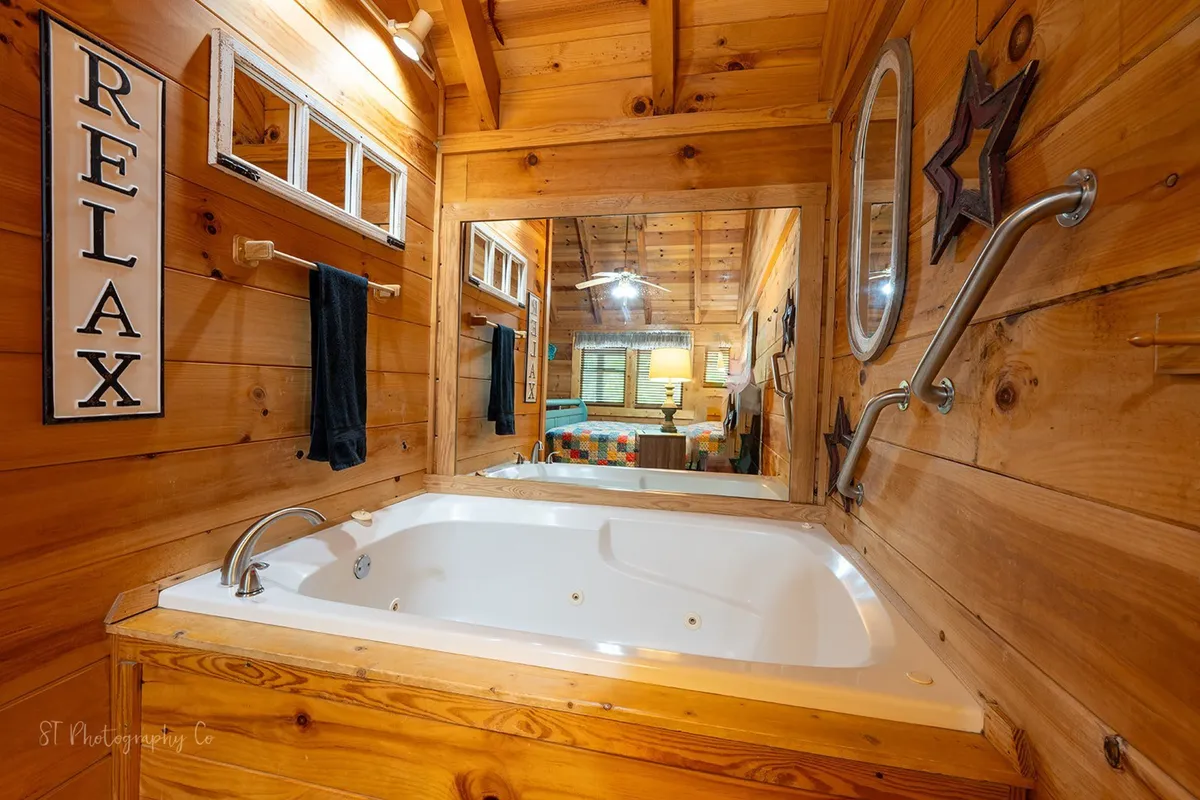 A spa-like bathroom space featuring a luxurious Jacuzzi tub surrounded by wooden walls, a 'relax' sign, and a mirror. The tub is inviting and exudes a calm, peaceful mood, ideal for soaking after a mountain adventure.