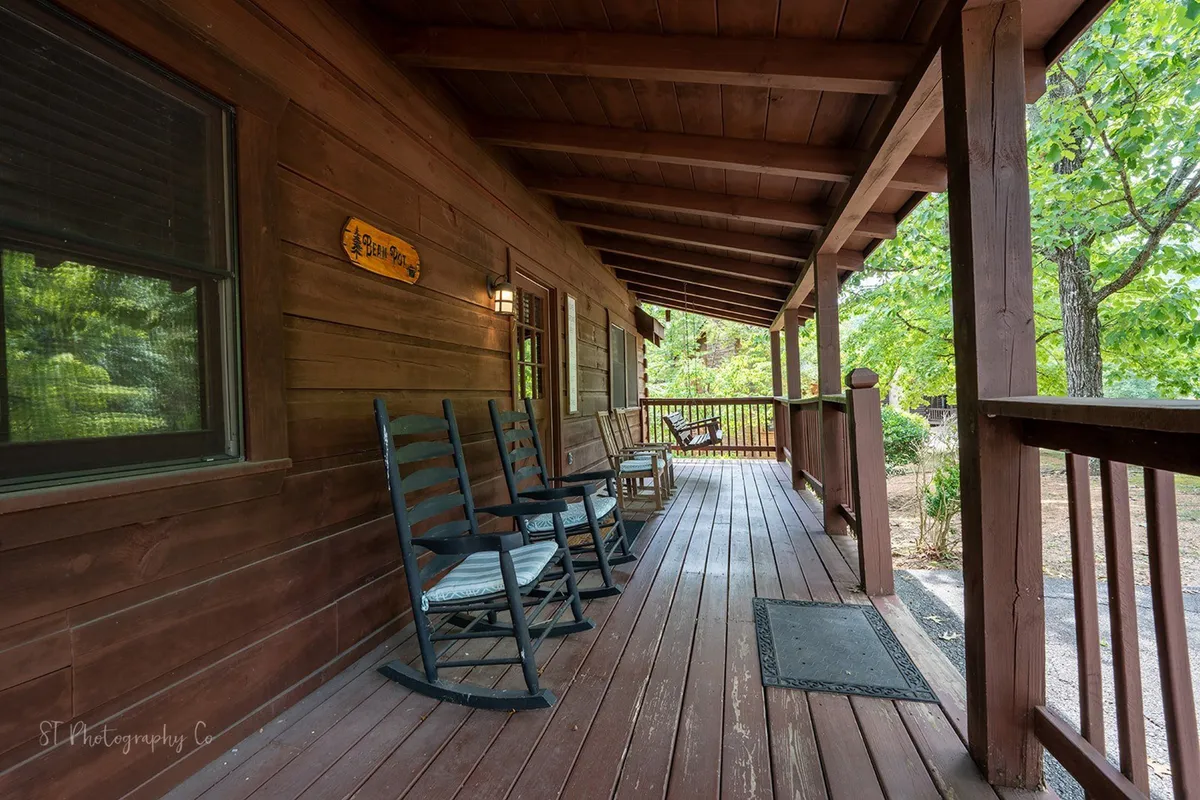 An inviting wooden porch features classic rocking chairs facing beautiful nature views, inviting guests to sit and unwind. The exterior setting is framed by lush greenery and a welcoming atmosphere, perfect for enjoying a morning coffee or evening conversation with loved ones.