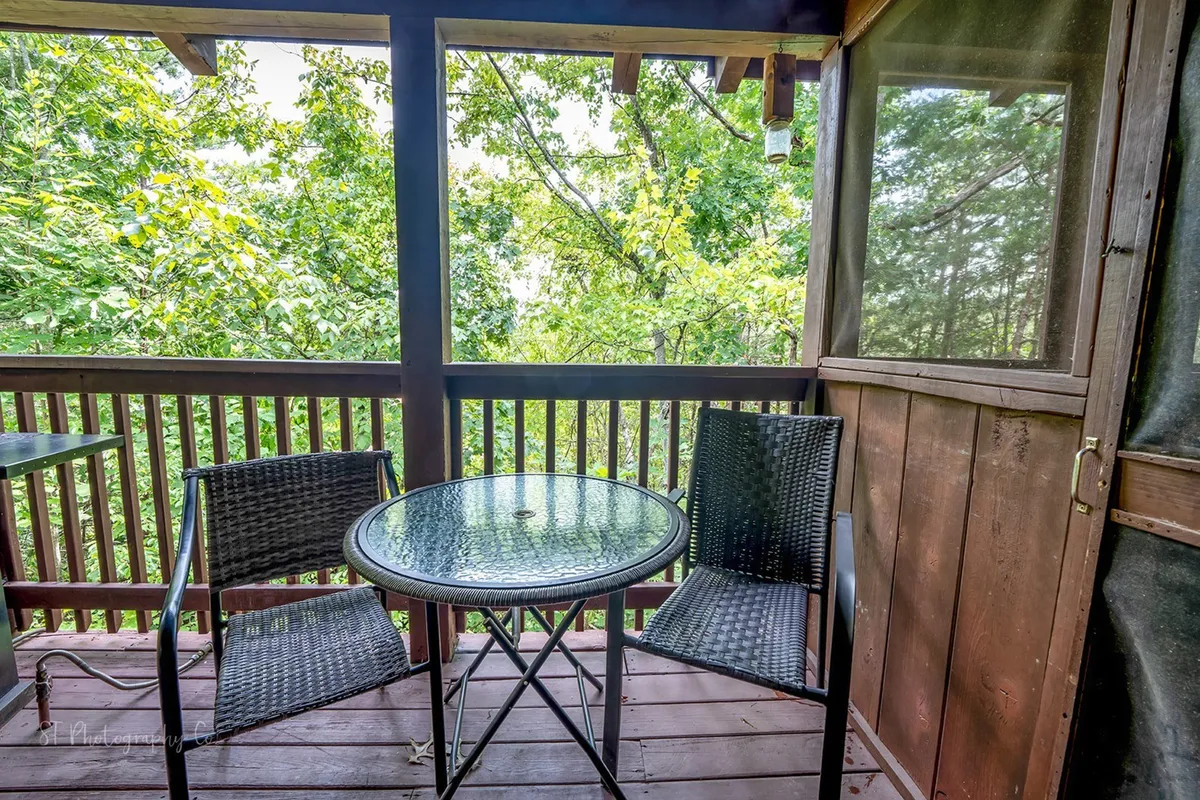 This image captures a serene screened-in porch with a round glass table and two wicker chairs, backed by lush greenery. The space is perfect for relaxing after a day out, enjoying coffee, or planning the next family adventure together.