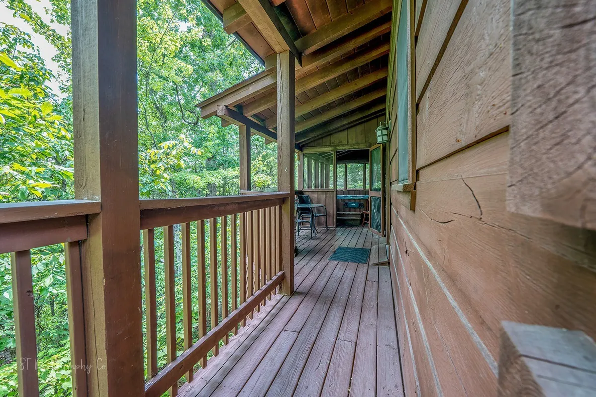 The image presents a serene exterior view of a wooden porch with railings, surrounded by lush greenery. The outdoor seating area suggests a tranquil space for couples to enjoy the fresh mountain air, morning coffee, or evening star-gazing together.