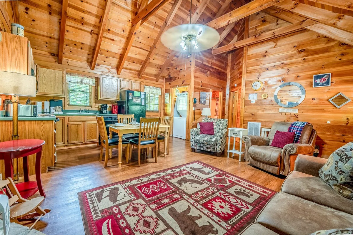 An inviting living and dining area with rustic wooden beams, a colorful area rug, a family-sized dining table, and a cozy seating area—ideal for family meals, board games, and movie nights after exploring Pigeon Forge.