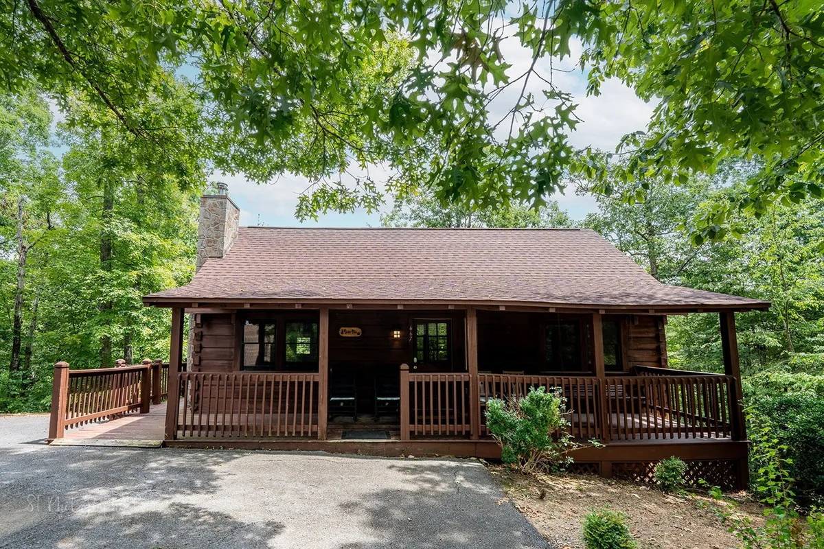 This image showcases the welcoming exterior of the Bean Pot, featuring a wooden porch, a stone chimney, and lush surrounding greenery. The inviting front door and expansive porch suggest a comfortable home base for families returning from adventures in Pigeon Forge.