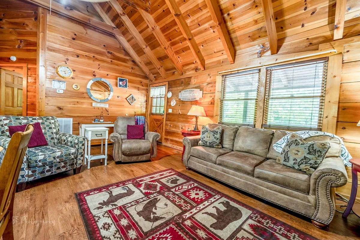 A welcoming living area with exposed wooden beams, a comfortable sofa, armchairs, and a colorful rug. The space is designed for relaxation and socializing, with thoughtful decor and an inviting, open layout that exudes warmth and charm.